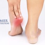 Person holding a painful heel, highlighting foot pain relief solutions. Premier Therapy Solutions logo in the background.