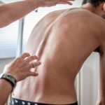 a man with scoliosis bending over in a physical therapist's office
