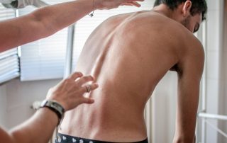a man with scoliosis bending over in a physical therapist's office