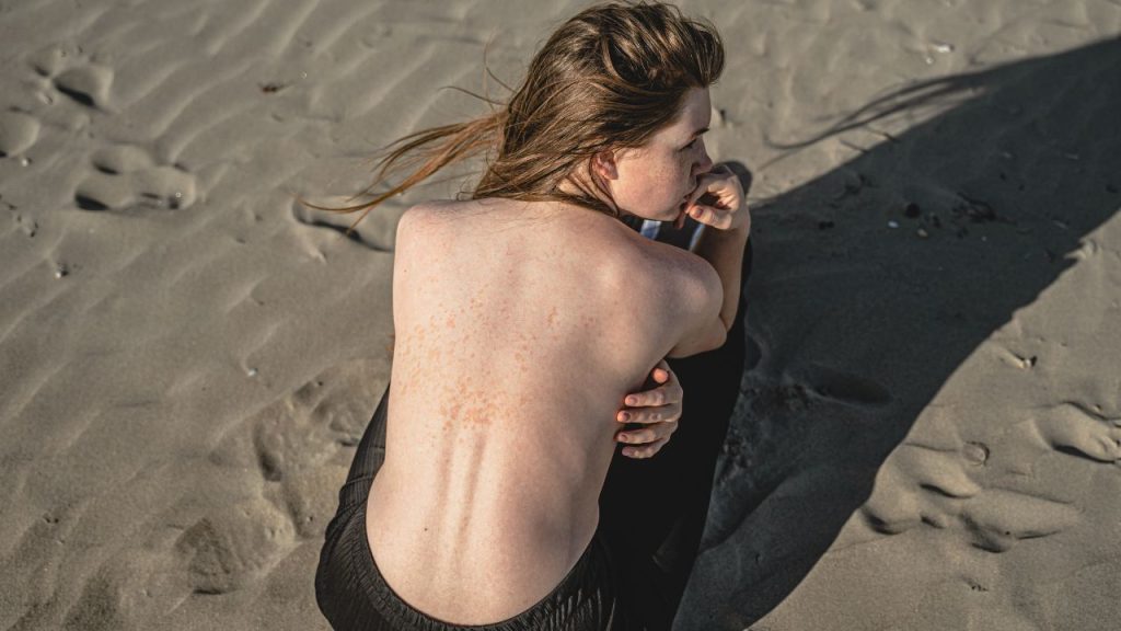 a woman with scoliosis sitting on the beach with her shirt off