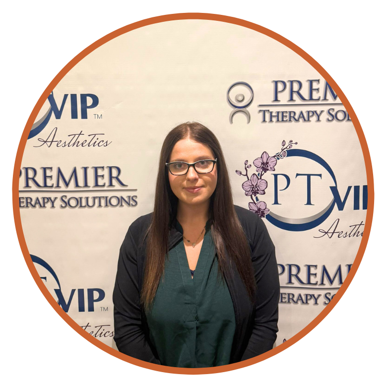 Amanaada Woman standing in front of Premier Therapy Solutions backdrop, wearing glasses and a green top, smiling confidently.
