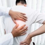 Physical therapist examining patient's back pain with hands, focusing on spine treatment and relief.