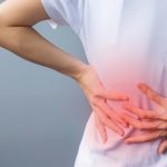 Person holding lower back in pain, indicating eds and scoliosis, with a red highlighted area on the back.
