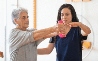 Senior woman performing arm strengthening exercises with assistance from therapist